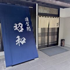 福岡県遠賀郡水巻町の「鮨 昭和」の正面玄関写真。大きな紺色の店頭幕と白い暖簾が掲げられた外観