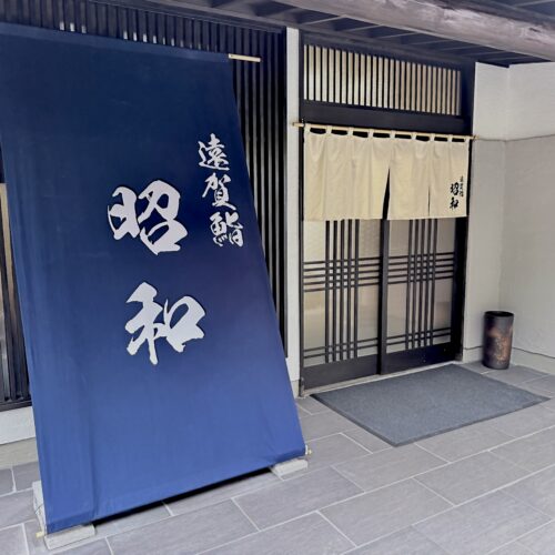 福岡県遠賀郡水巻町の「鮨 昭和」の正面玄関写真。大きな紺色の店頭幕と白い暖簾が掲げられた外観