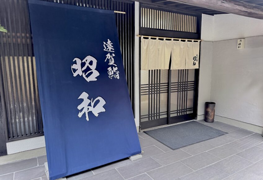 福岡県遠賀郡水巻町の「鮨 昭和」の正面玄関写真。大きな紺色の店頭幕と白い暖簾が掲げられた外観