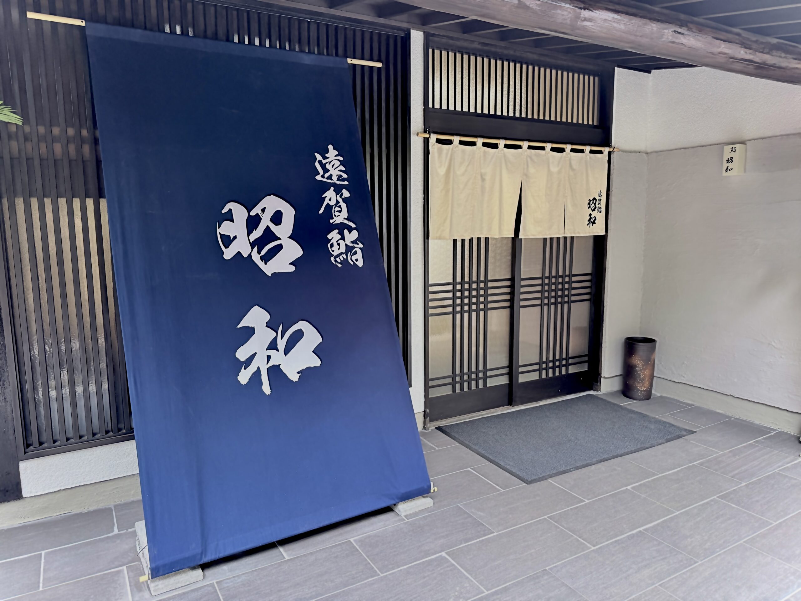 福岡県遠賀郡水巻町の「鮨 昭和」の正面玄関写真。大きな紺色の店頭幕と白い暖簾が掲げられた外観